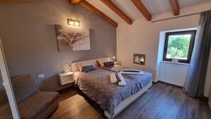 Een slaapkamer met een groot bed, een nachtkastje, een wandlamp, een raam met gordijnen en een houten plafond.