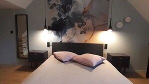 A bedroom with a large bed, two bedside tables, a wall-mounted artwork, and a sloped ceiling. - La Petite Bélérit, town house - Landerneau (Landerneau)