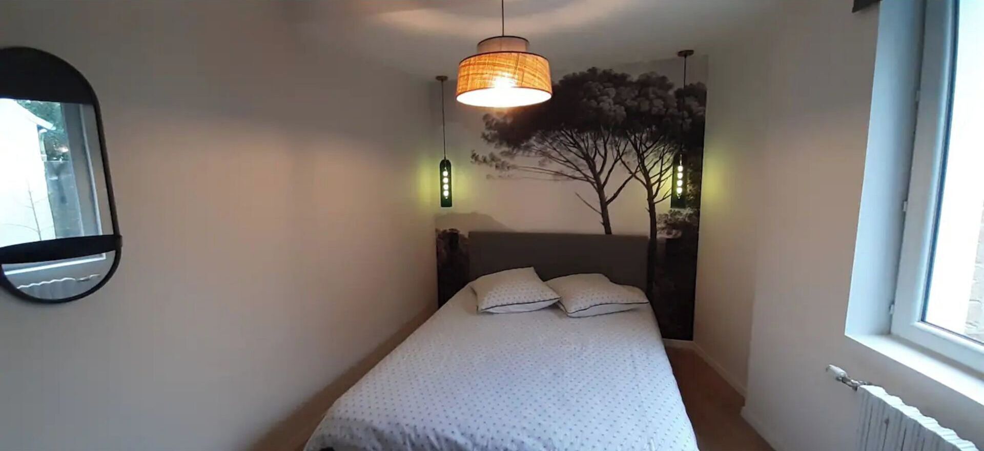 Een slaapkamer met een bed, een hanglamp, een spiegel aan de muur en een raam.