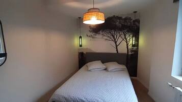 Een slaapkamer met een bed, een hanglamp, een spiegel aan de muur en een raam.