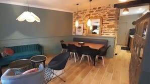 A cozy living area with a blue sofa, a small round table, and a pet bed. There is a dining table with chairs and a stone wall with a mirror above it. - La Petite Bélérit, town house - Landerneau (Landerneau)