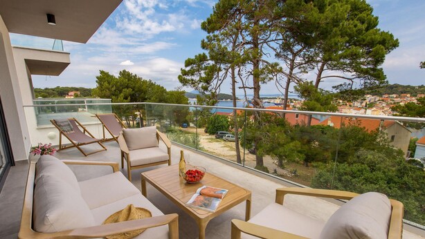 A balcony with outdoor furniture, a table with a magazine, and a view of the sea and buildings. - Beach front apartment in Mali Losinj with WiFi (Mali Losinj)