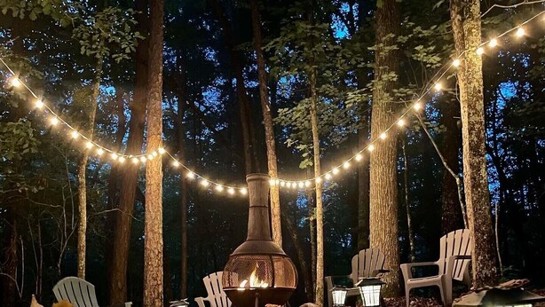 An outdoor seating area with Adirondack chairs, a fire pit, and string lights. - Mountain Cabin with creek and hiking trail! Minutes from Blue Ridge (Morganton)
