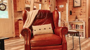 A cozy wooden cabin interior with a leather armchair, a bookshelf, and a dining table. - Mountain Cabin with creek and hiking trail! Minutes from Blue Ridge (Morganton)