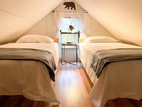 Un dormitorio acogedor en el ático con dos camas, una mesita pequeña y una ventana decorada con la silueta de un oso.