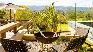 Un espacio al aire libre con mesa de madera, dos sillas, una mecedora y una planta en maceta.