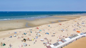 A beach with numerous sunbeds and umbrellas, a clear sky, and a calm sea.