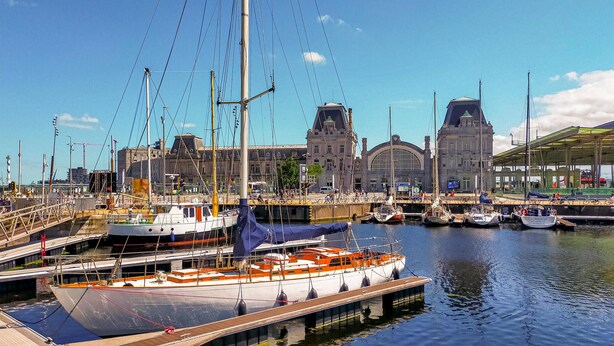 A marina with boats docked, a large building with a green roof, and a bridge.