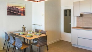A dining area with a wooden table set for four, surrounded by modern chairs. A painting hangs on the wall above the table.