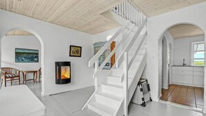 A spacious room with a white staircase, a fireplace, a dining area with chairs, and a kitchen with a window. - Gorgeous home in Vestervig with WiFi (Vestervig)