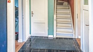 Un couloir doté d’un sol carrelé de carreaux noirs, d’une porte blanche ornée d’une bande verte et d’un escalier menant à un palier.