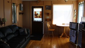 Un espacio habitable pequeño con un sofá de cuero negro, una mesa de comedor de madera y un refrigerador.