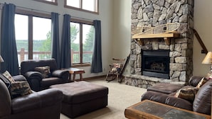 A cozy living room with a stone fireplace, leather sofas, and large windows overlooking a deck. - Biwabik Bunkhouse near Giants' Ridge (Aurora)