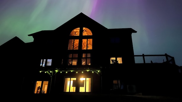 A house with a large arched window and multiple smaller windows, under a night sky with visible aurora borealis. - Biwabik Bunkhouse near Giants' Ridge (Aurora)