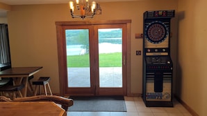 A room with a wooden table, chairs, a dartboard, and a view of a lake through glass doors. - Biwabik Bunkhouse near Giants' Ridge (Aurora)
