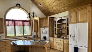 A kitchen with wooden cabinets, a central island with stools, a refrigerator, and a window with curtains. - Biwabik Bunkhouse near Giants' Ridge (Aurora)
