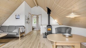 A cozy loft bedroom with a sloped ceiling, a built-in wood-burning stove, a gray sofa, a wooden dining table, and a view of the outdoors. - Gorgeous home in Gråsten with sauna (Gråsten)
