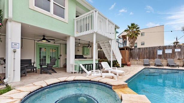 A swimming pool area with a hot tub, outdoor seating, and a covered patio.