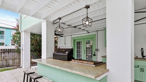 A covered outdoor kitchen area with a bar counter, stools, and a grill.