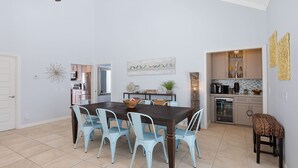 A dining area with a dark wooden table and light blue chairs, a ceiling fan, and a kitchen in the background.