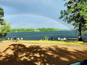 A lakeside view with a picnic area, benches, and a tree.