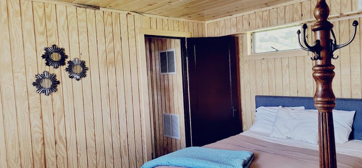 A wooden-paneled room with a bed, a window, and wall-mounted air vents.