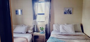 Ein Zimmer mit zwei Betten, einem kleinen Tisch mit Lampe, einer Topfpflanze und einer Wand-Klimaanlage.