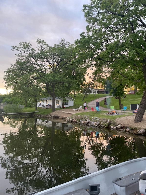 A lakeside setting with a dock, a small docked boat, and a grassy area with outdoor seating.