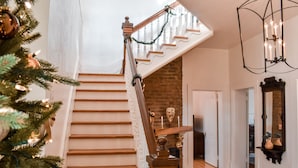 Eine Treppe mit hölzernem Geländer und weißen Spindeln, die zu einem Raum mit Backsteinwand und Tür führt.