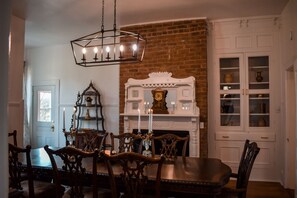 A dining room with a brick fireplace, white cabinets, and a chandelier. - New! Large Victorian home! Outdoor space for entertaining! (Sevierville)
