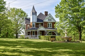 A large, two-story house with a prominent tower, a wrap-around porch, and a well-manicured lawn. - New! Large Victorian home! Outdoor space for entertaining! (Sevierville)