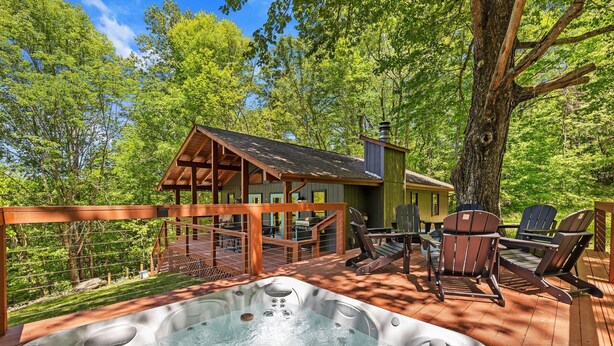 A hot tub on a wooden deck with outdoor furniture, surrounded by trees.