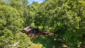 A cabin surrounded by dense forest, with a deck and outdoor seating area.