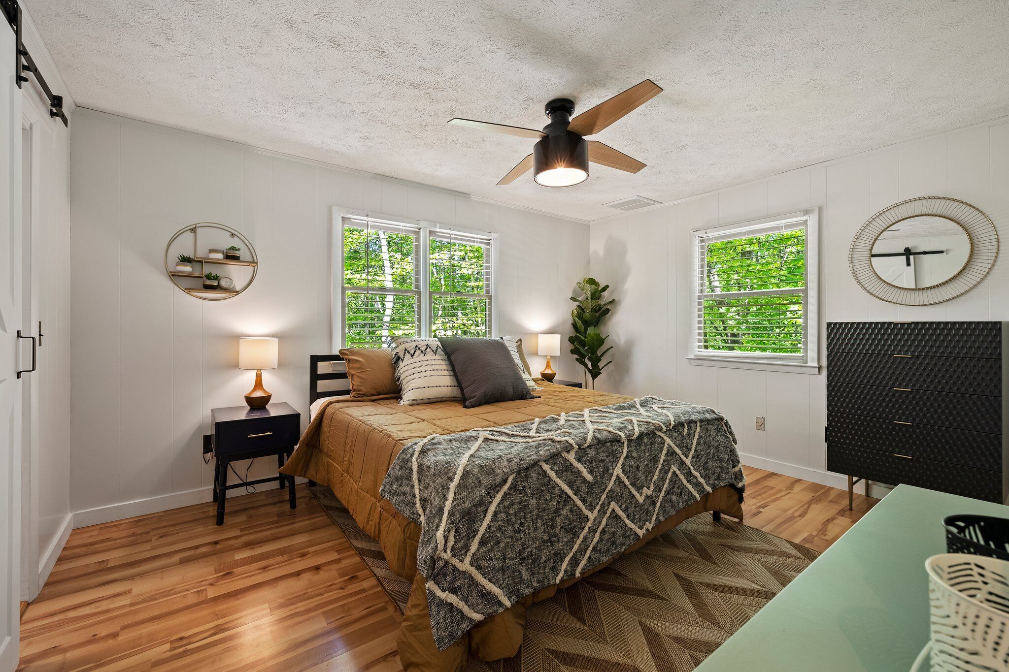 A bedroom with a bed, bedside tables, a ceiling fan, windows, and a dresser.