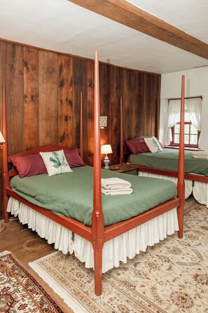 A four-poster bed with a wooden frame, green bedding, and a white ruffled skirt.