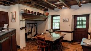 Una mesa de comedor de madera con sillas, un colgador para ollas y una ventana con vista a árboles.