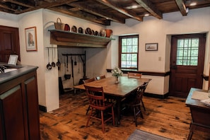 Et træbord med stole, en ophængt grydekrog og et vindue med udsigt til træer.