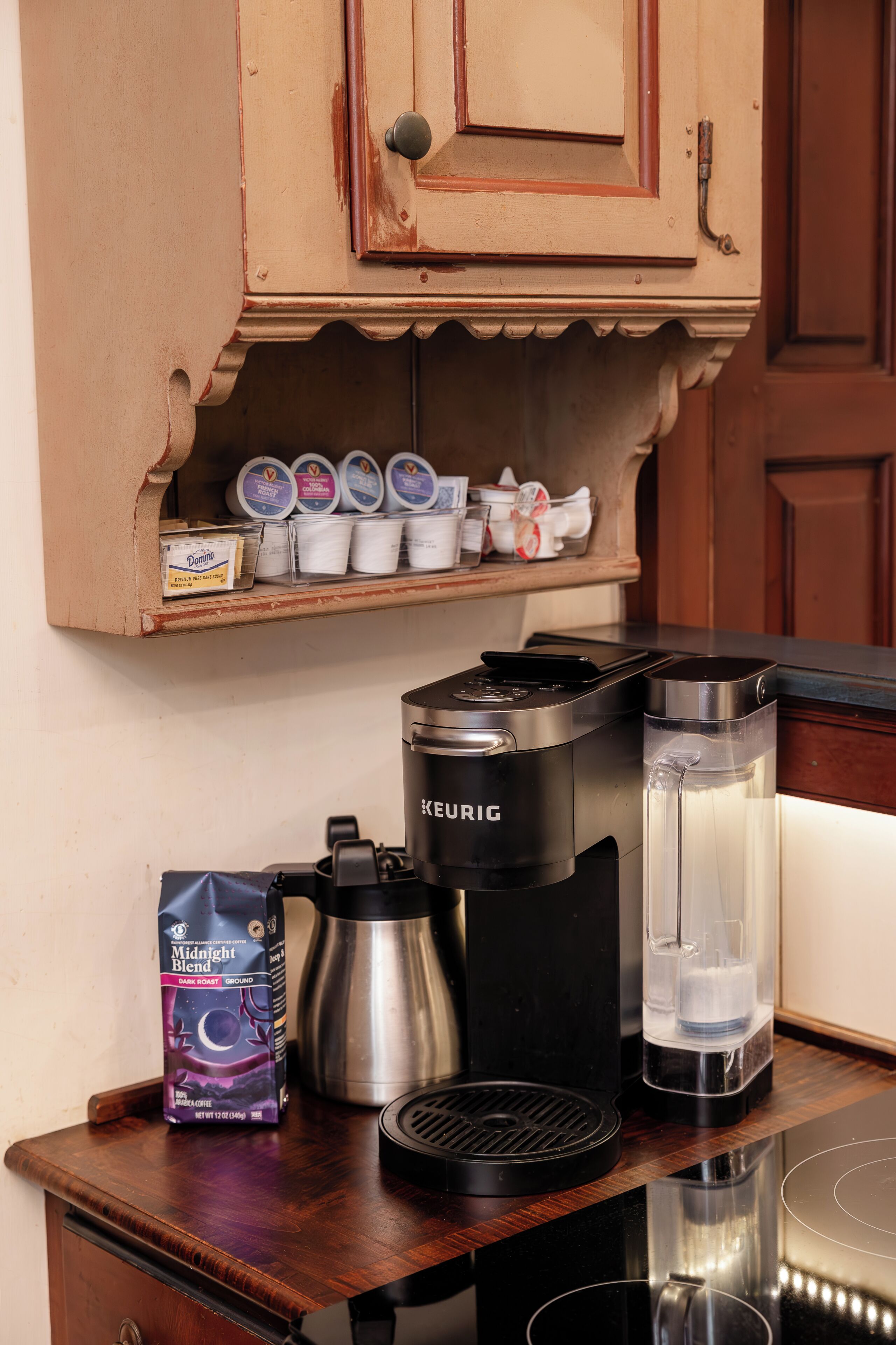Una encimera de cocina con una cafetera Keurig, una jarra de café, un dispensador de agua y un paquete de café.