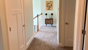 A hallway with carpeted flooring, white doors, and a wooden railing. - Cozy Modern Cottage Style Home minutes from VT, RU, Christiansburg Aquatic Cente (Christiansburg)