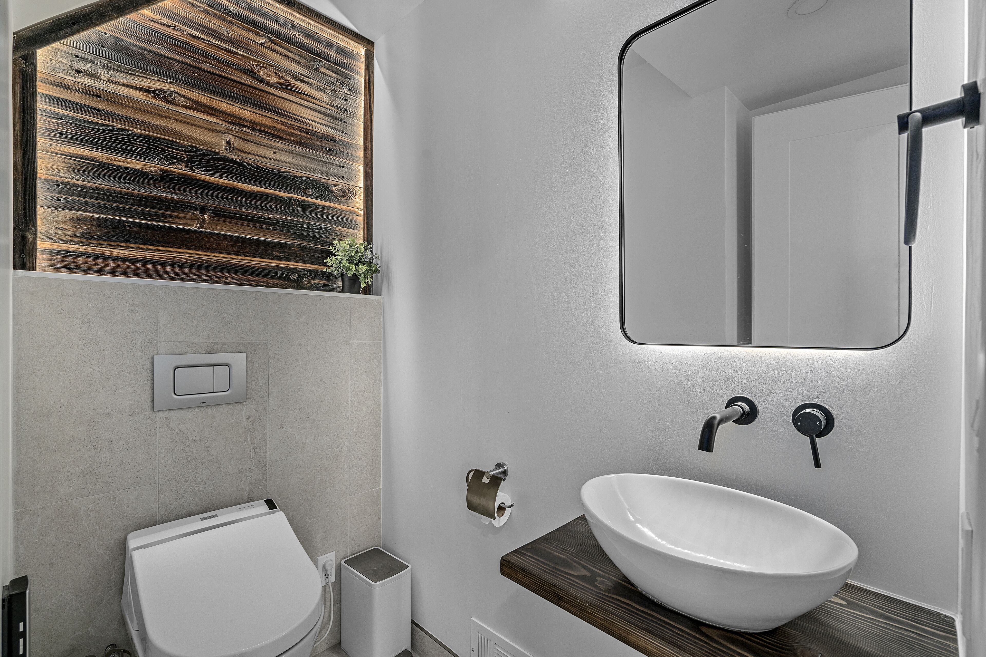 A modern bathroom with a wooden accent wall, a white sink, and a large mirror.