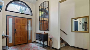 Un couloir avec une porte en bois, une grande fenêtre, un miroir et un escalier.