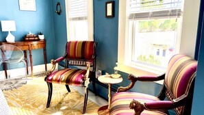 Une pièce avec un mur bleu, deux fauteuils à rayures, une petite table ronde, une chaise et une lampe.