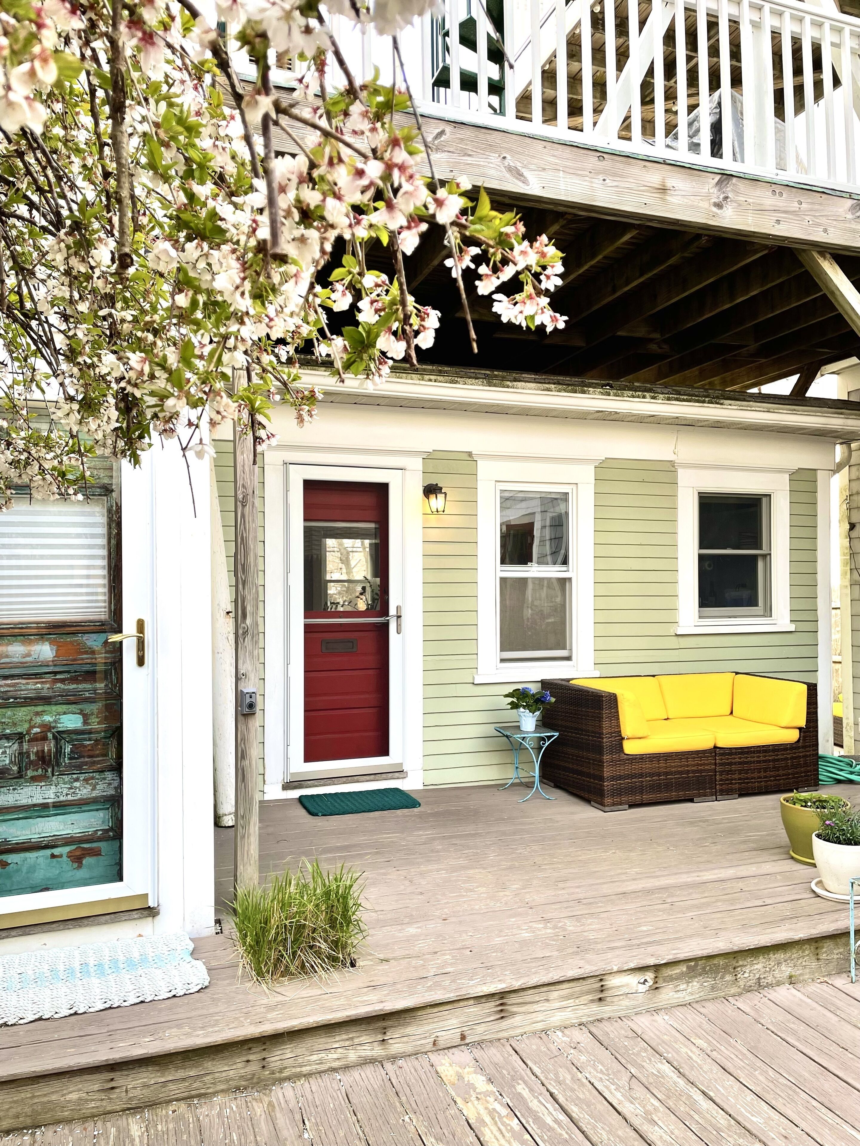 A house with a red door, a porch with a wicker sofa, and a wooden deck.