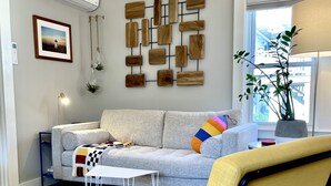 Un salon moderne avec un canapé gris, un fauteuil jaune, une œuvre d’art en bois fixée au mur, un tableau encadré et une plante en pot.