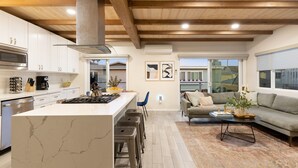 Una cocina moderna con armarios blancos, una isla de mármol y una campana extractora central.