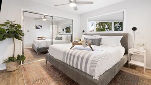 Un dormitorio moderno con una cama grande, un ventilador de techo, una mesita de noche y una ventana con persianas.