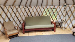 A cozy interior of a yurt with a wooden sofa, a wooden chair, and a blue mat on the floor.