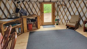 A cozy interior of a yurt with a wooden desk, chairs, and a large mat on the floor.