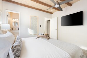 Un dormitorio con una cama grande, un televisor de pantalla plana montado en la pared, un ventilador de techo y techo de madera.