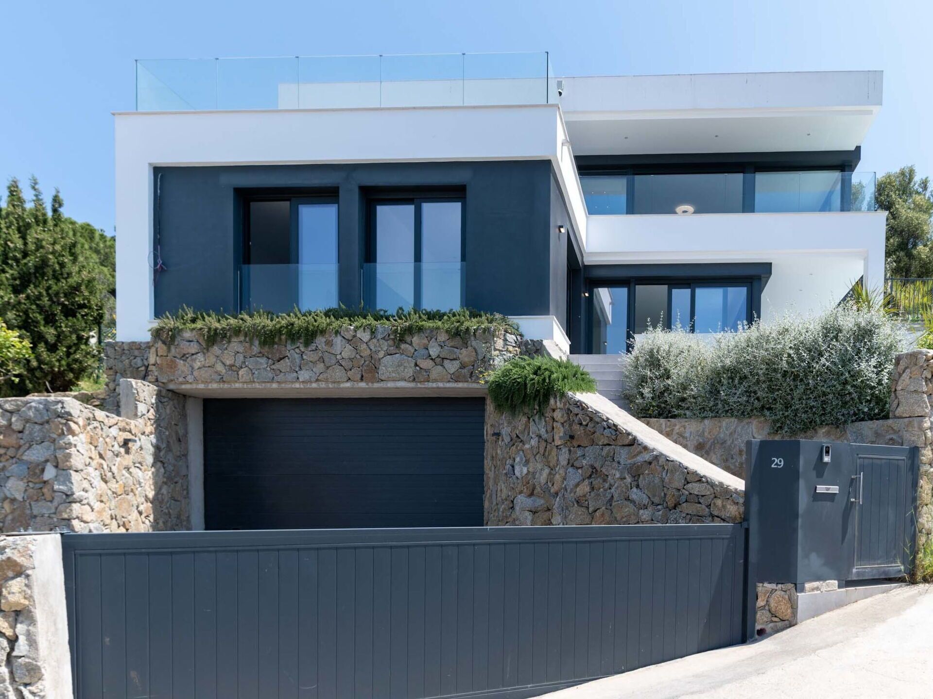 A modern two-story house with a stone facade, large windows, and a gated entrance.